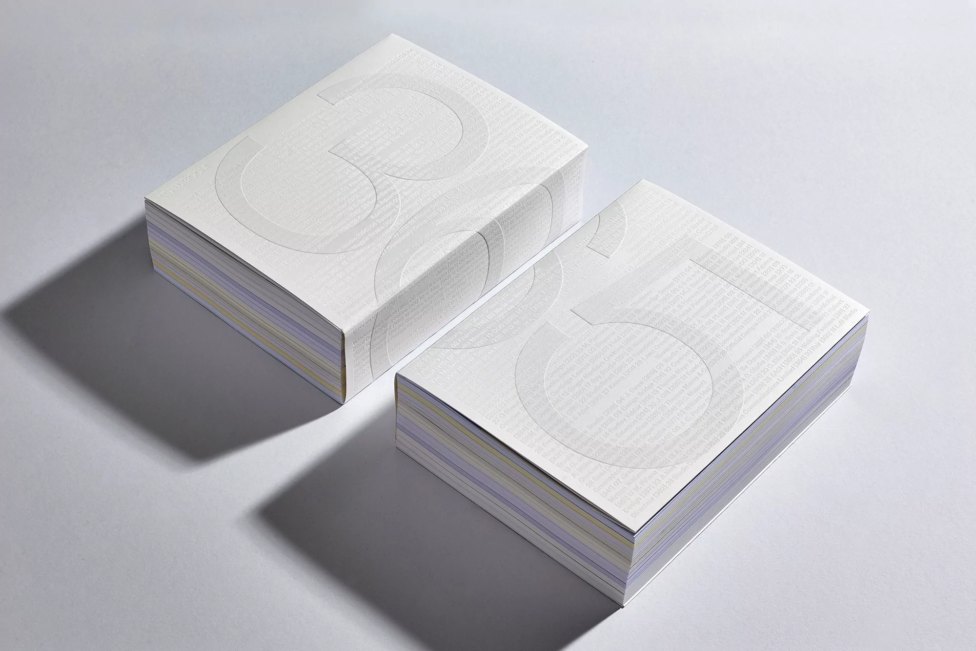 Two stacks of white paper with a large number 35 printed on the covers, set on a white surface and casting shadows.