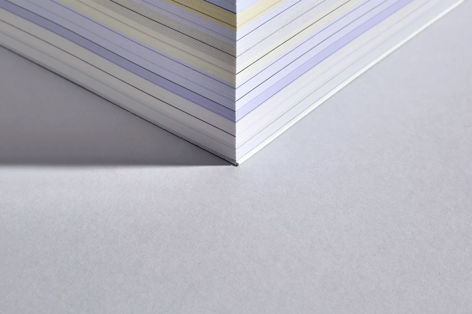 Close-up shot of a book's corner with paper edges visible, showcasing a blend of light and dark shadows on a textured surface.