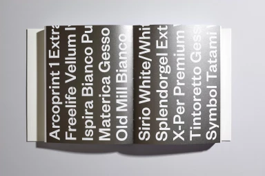 An open paper swatch book displaying bold white typography on dark pages against a clean grey background