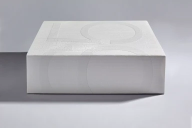 White embossed paper box with typography details resting on a clean studio surface casting a shadow