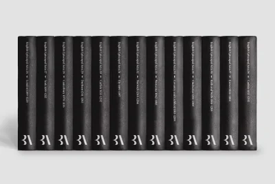 A row of twelve black leather-bound books standing upright against a neutral grey background with white typography on spines.