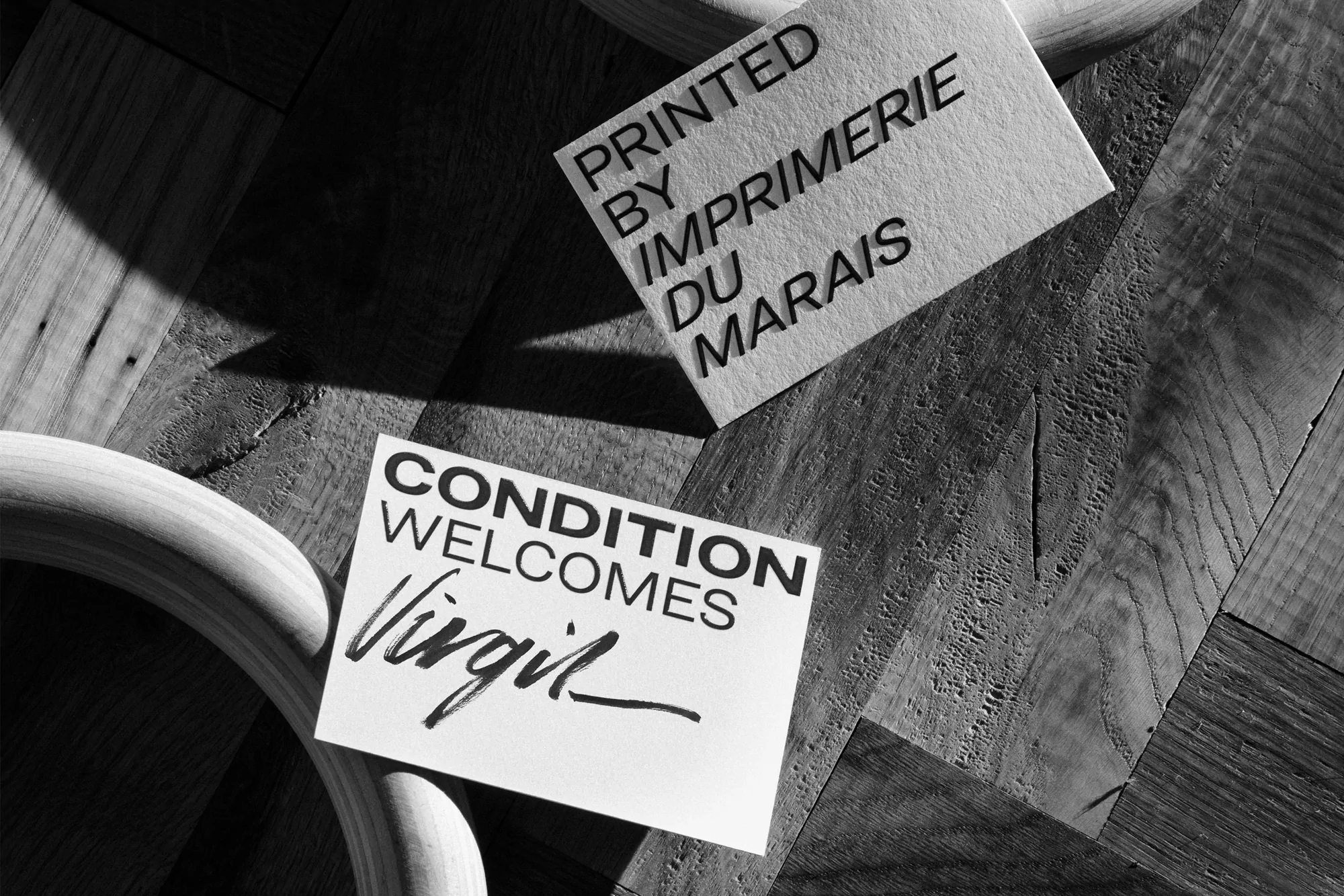 Two white cards with black text sit on a wooden surface beside a partial wooden circle, highlighting typography and material contrast.