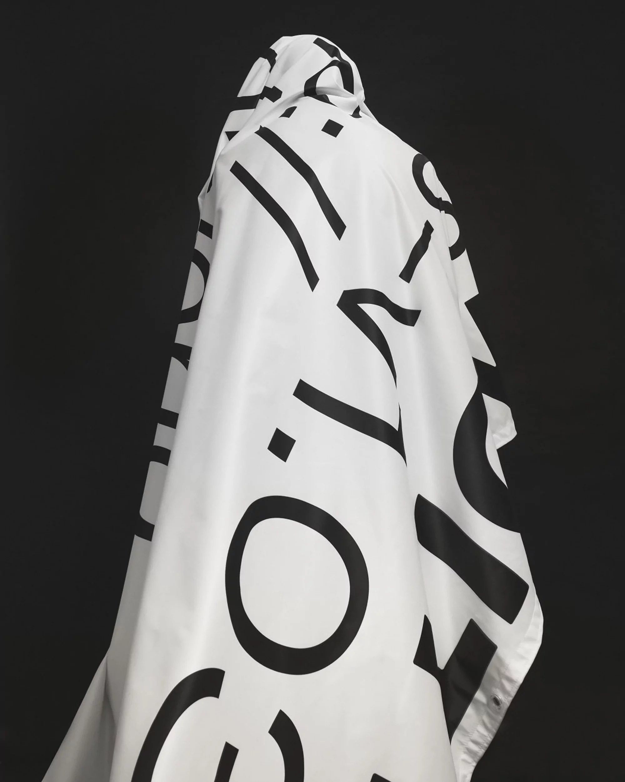 Person cloaked in white fabric with black text against dark background, evoking minimalist fashion and striking visual design.