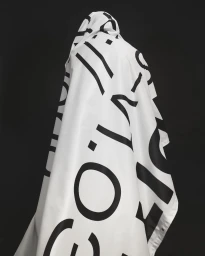 Figure draped in white fabric printed with large black typographic letters against dark background