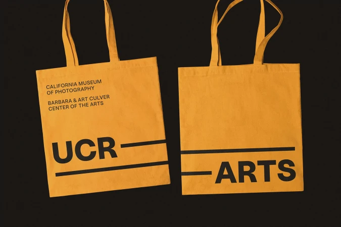 Two yellow tote bags with black text featuring 'California Museum of Photography' and 'UCR ARTS' on a dark background.