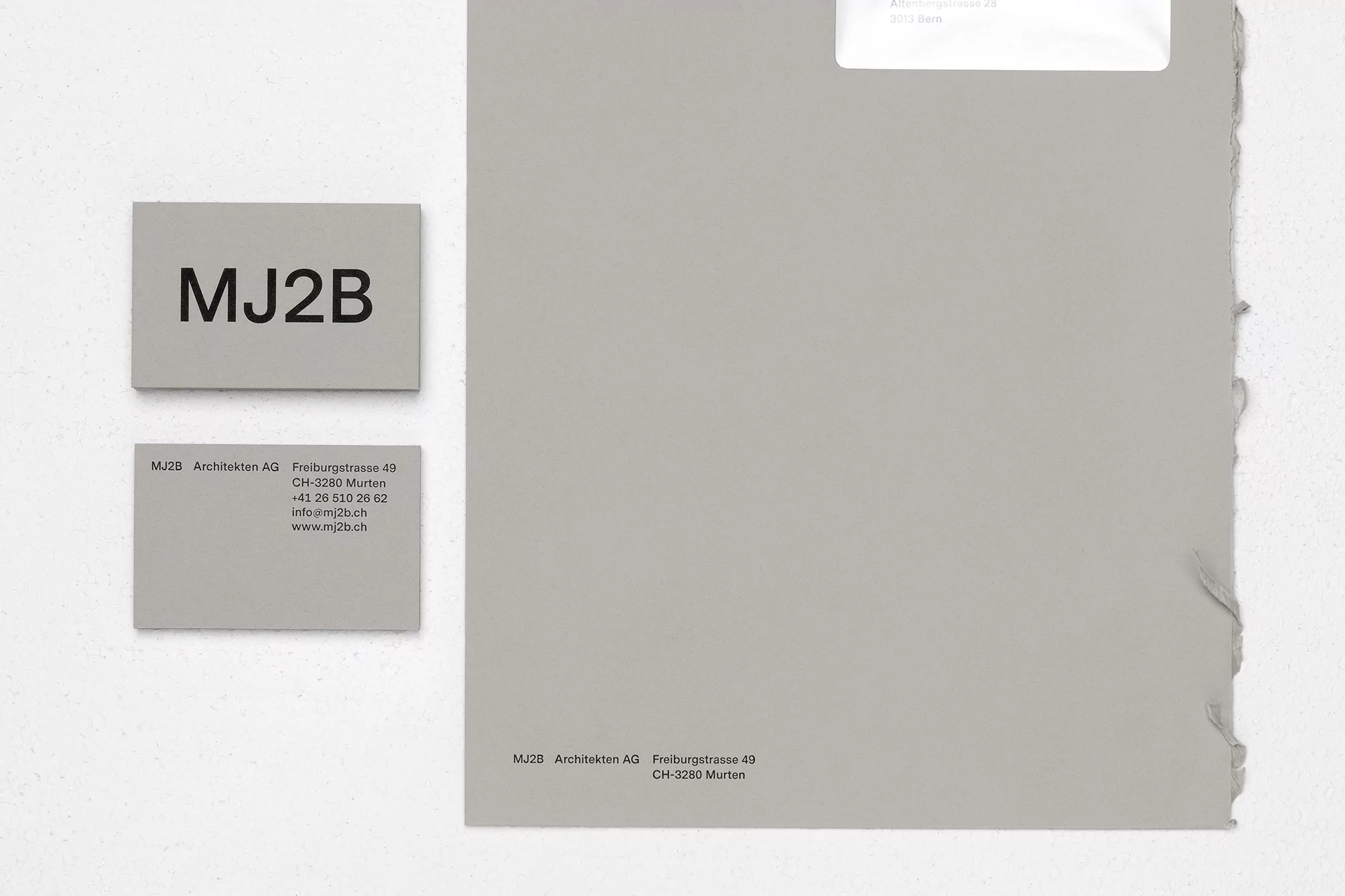 Close-up of grey paper samples and business cards featuring the logo and contact information for MJ2B Architekten AG.