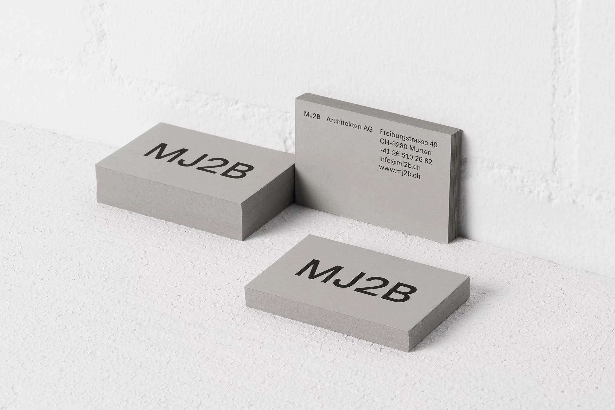 Three stacks of grey business cards displaying the company name and contact details, set against a clean white background.