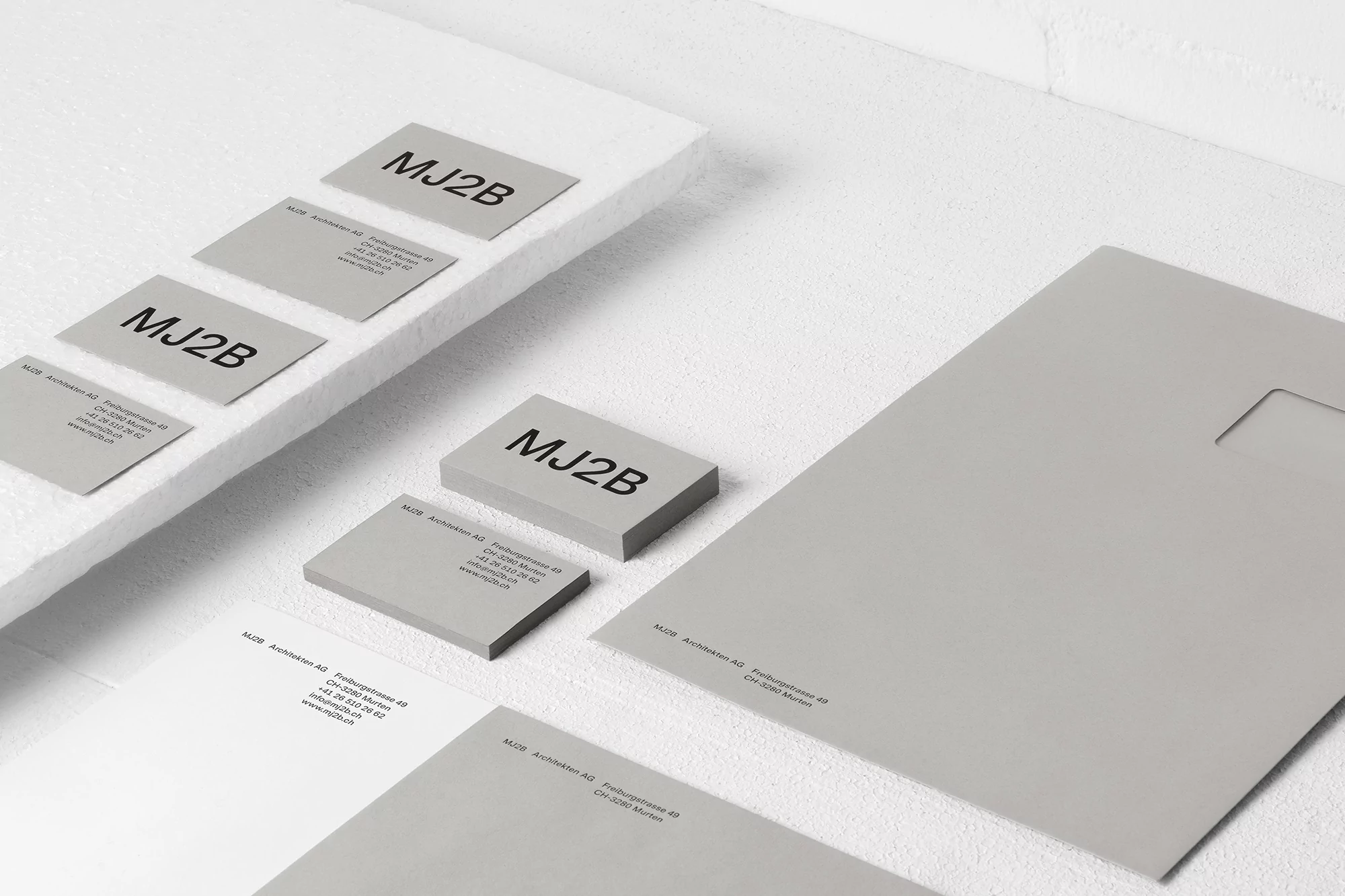 Elegant, minimalist product shot of business cards, stationery, and a letterhead featuring the logo MJ2B against a white surface.