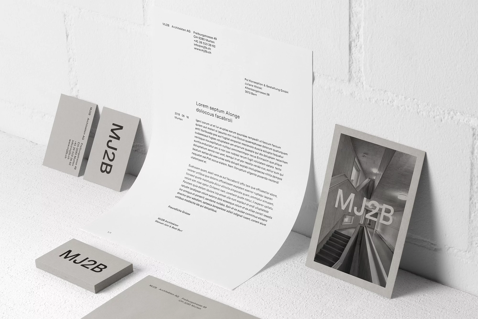Letterhead, business cards, and card with architectural image featuring the brand MJ2B, arranged against a white brick background.