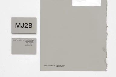 Minimalist graphic design stationery items including business cards and letterhead featuring MJ2B branding on grey paper.