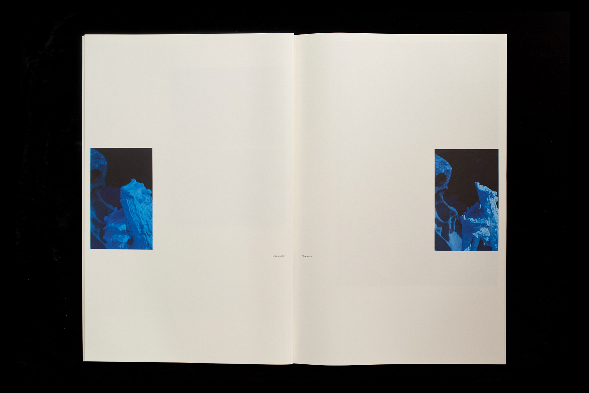 Open book with abstract blue images on white pages against a black background, creating a minimalist and artistic composition.