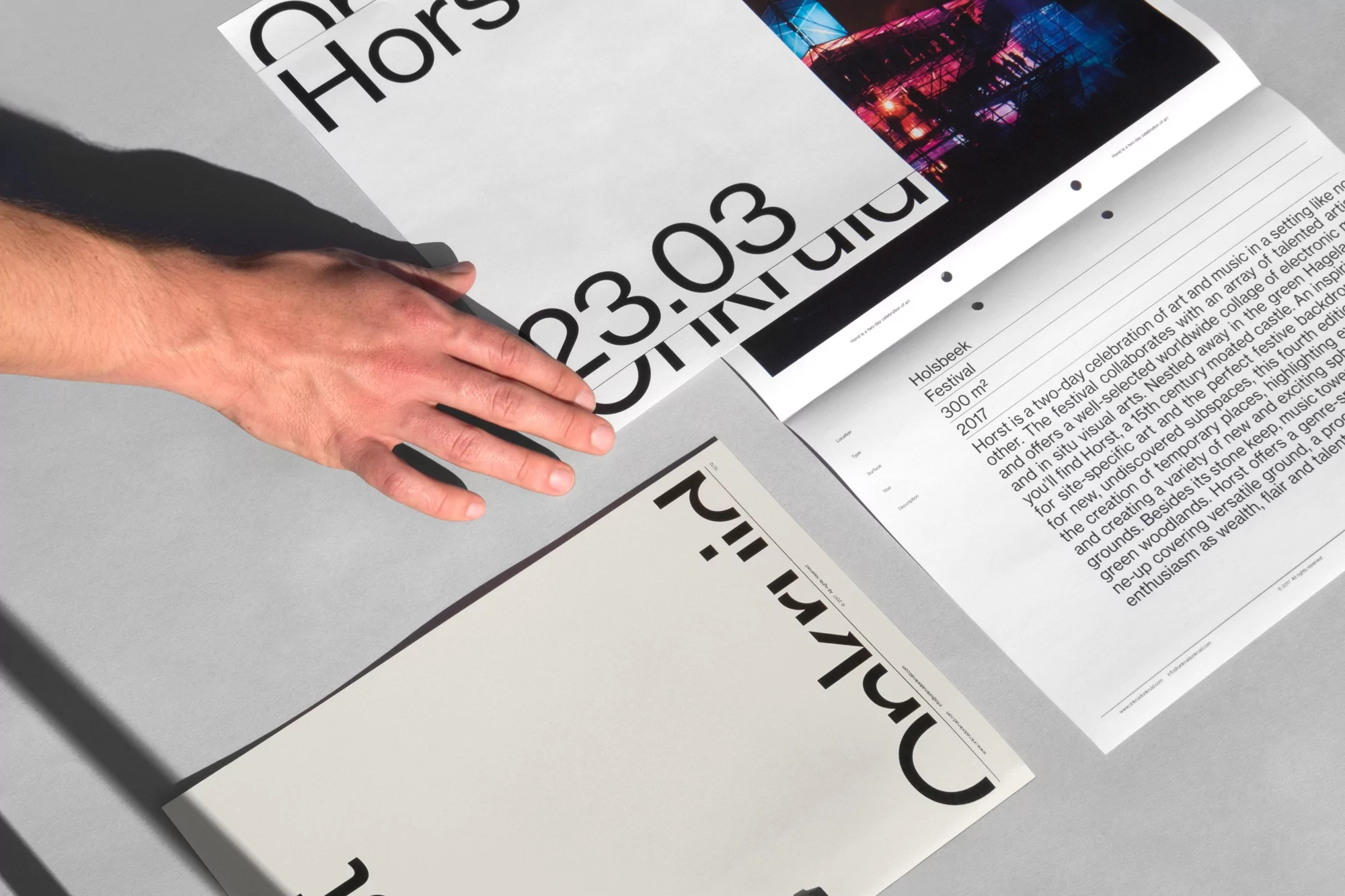 Hand interacting with Horst Festival promotional materials. Close-up on flyer designs featuring event details and artistic visuals.
