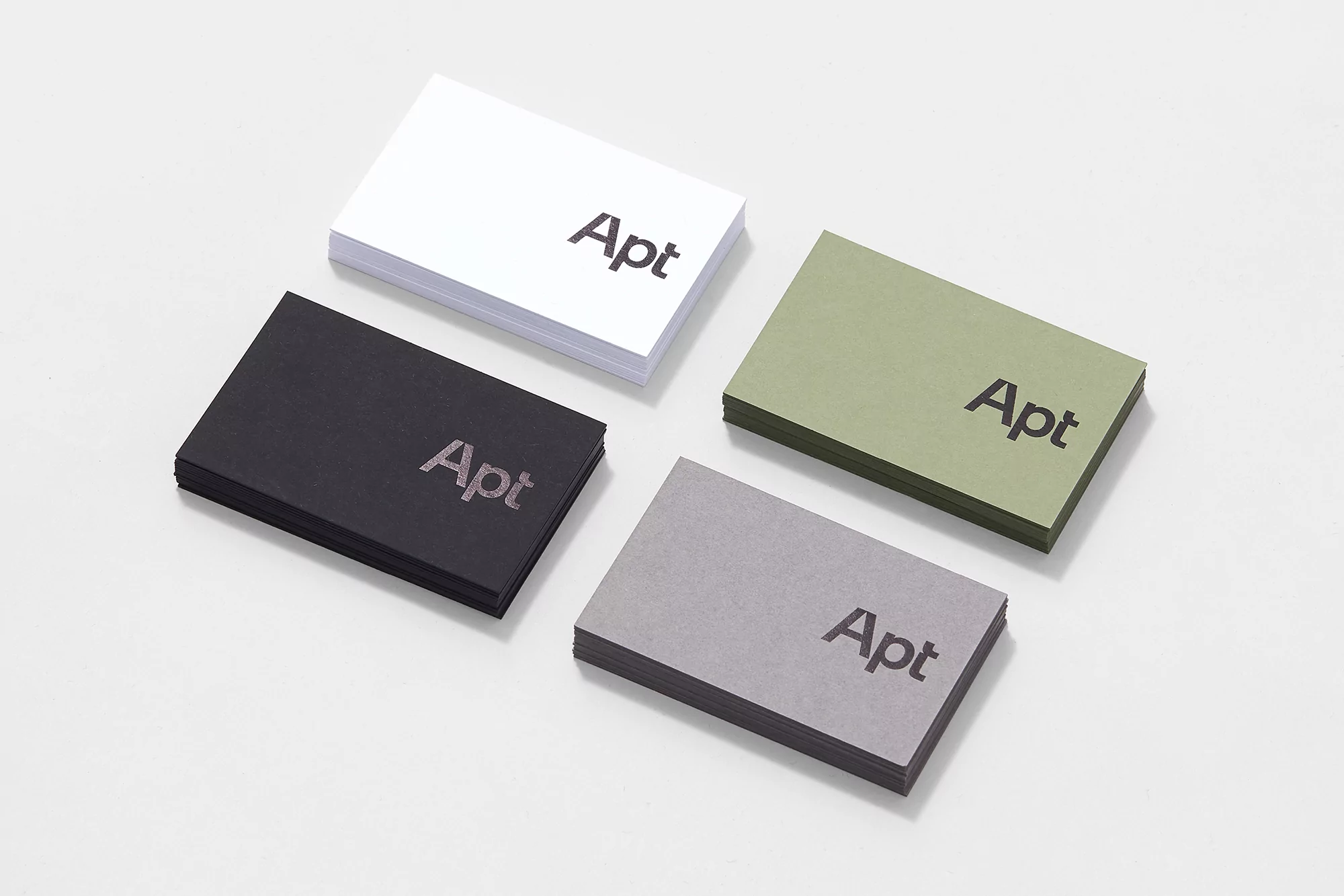 Four stacks of business cards in white, black, olive green, and grey arranged neatly on a plain white surface.