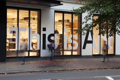 Exterior storefront featuring large white typographic lettering reading This is Apt across full-height glass windows.