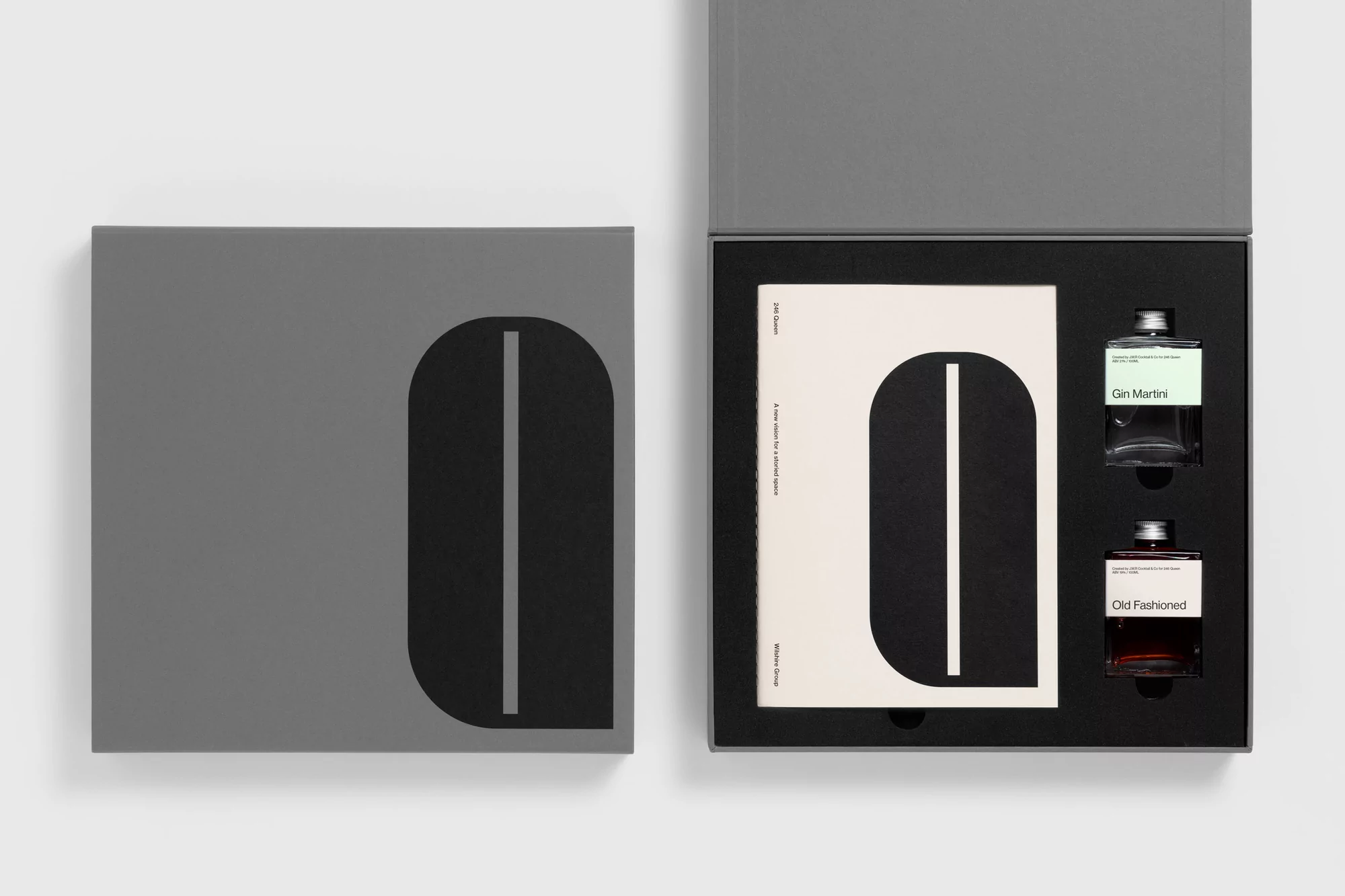 Two grey boxes, one opened, showcasing two small bottles and a booklet with a black and white design and minimal typography.