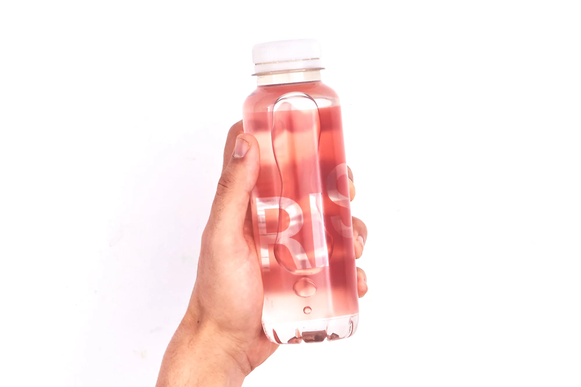 Hand holding a clear plastic bottle with a white cap, filled with a pink liquid, against a bright white background in a studio setting.