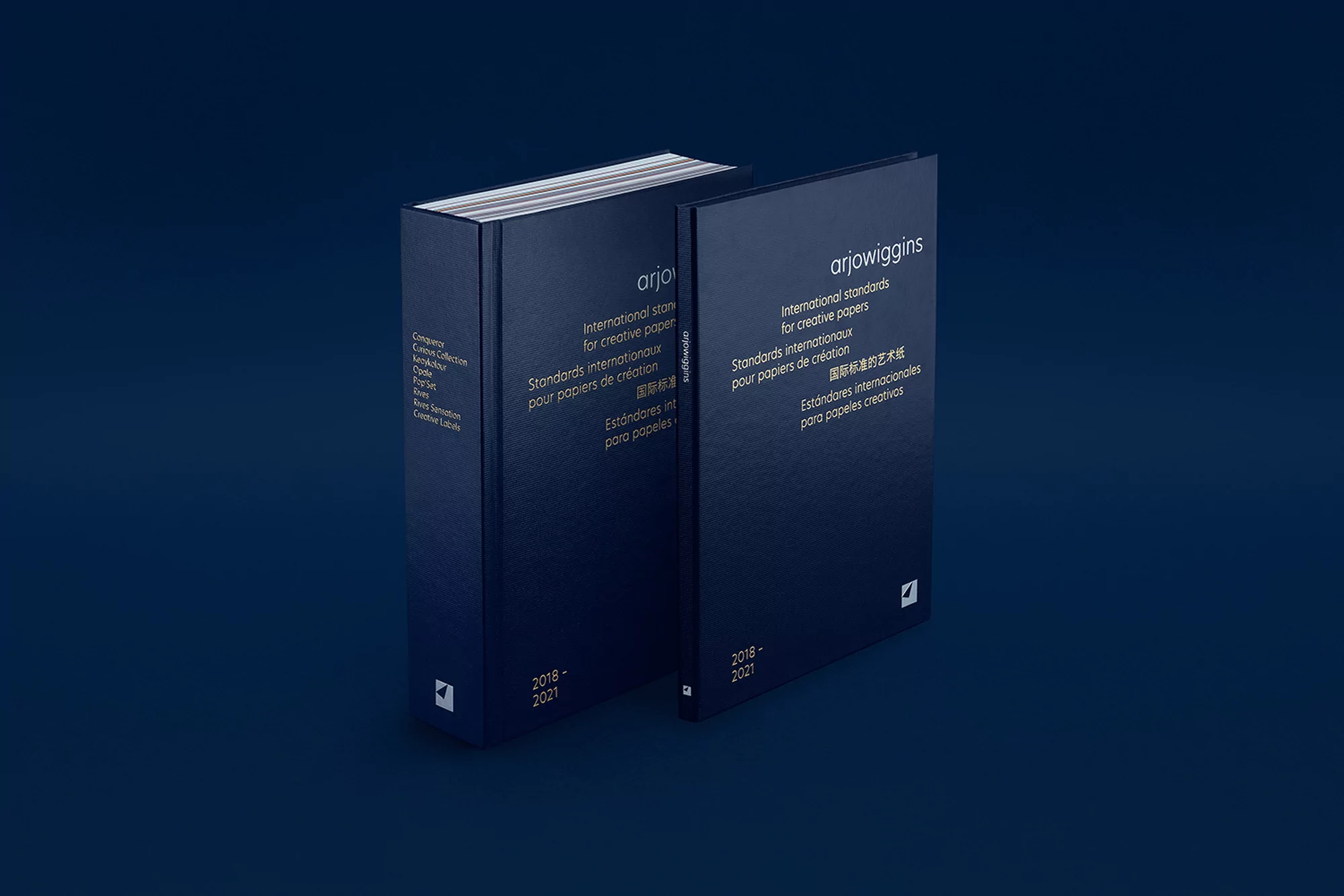 Two ArjoWiggins International Standards for Creative Papers books stacked against each other on a dark blue background, showcasing their covers.