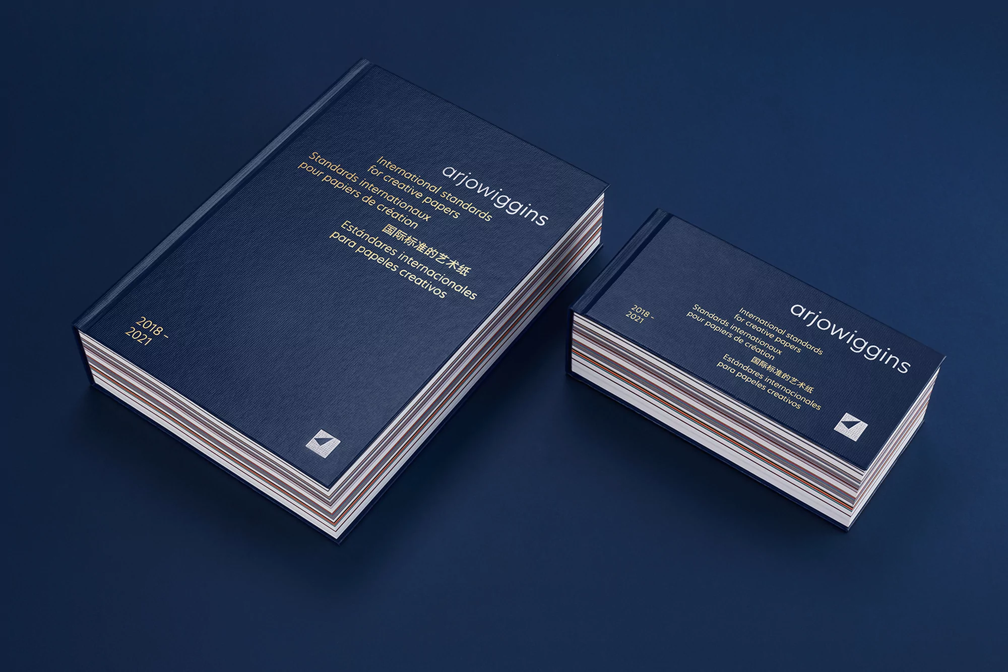 Two ArjoWiggins paper sample books in blue tones, one larger and one smaller, displayed on a blue surface.
