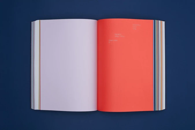 Open book on a dark blue surface, featuring an orange right-hand page with visible text and a violet-tinted left-hand page.