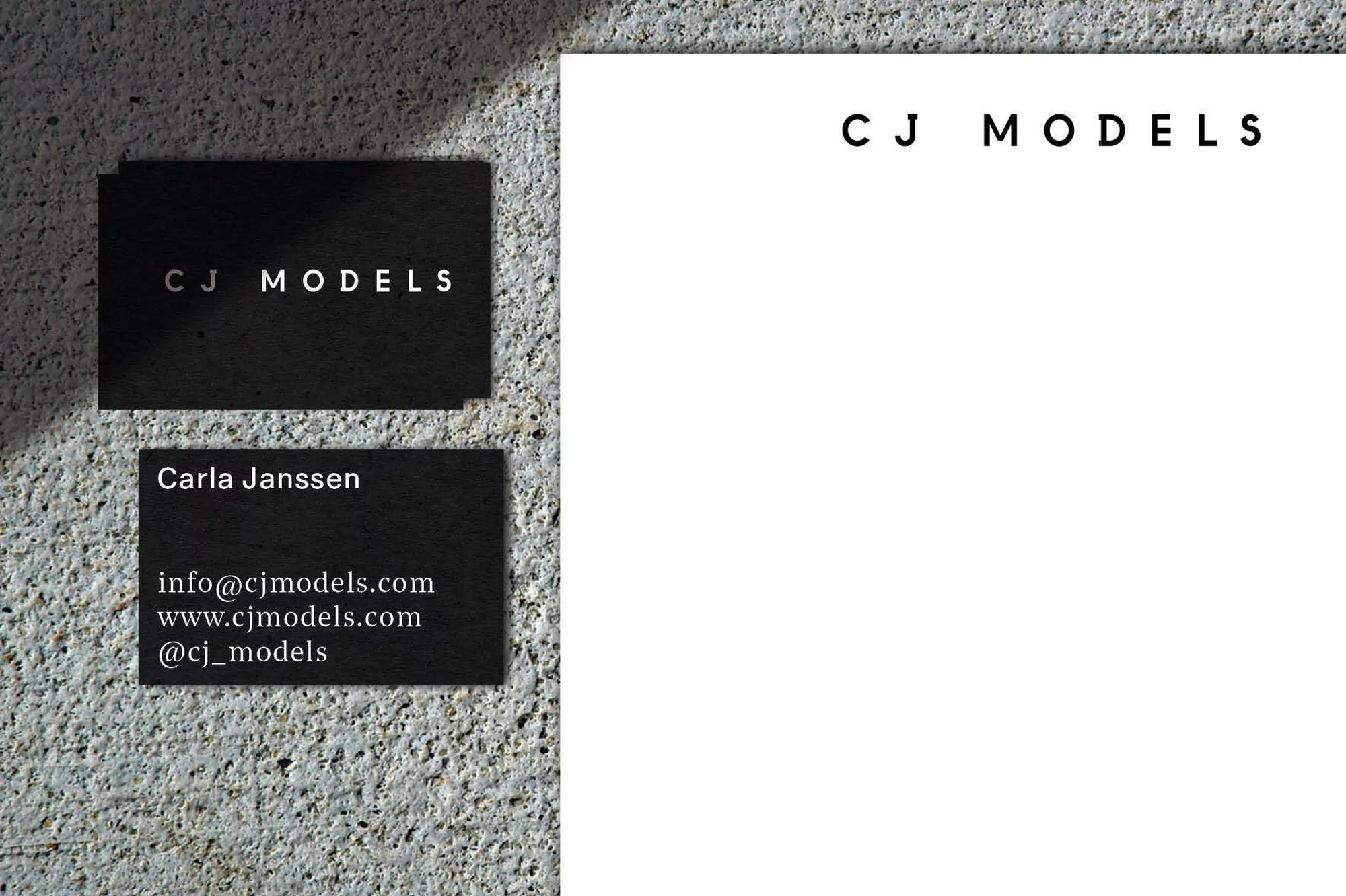 Stack of black business cards with white text, set on a mottled concrete surface next to a larger white card with black text.