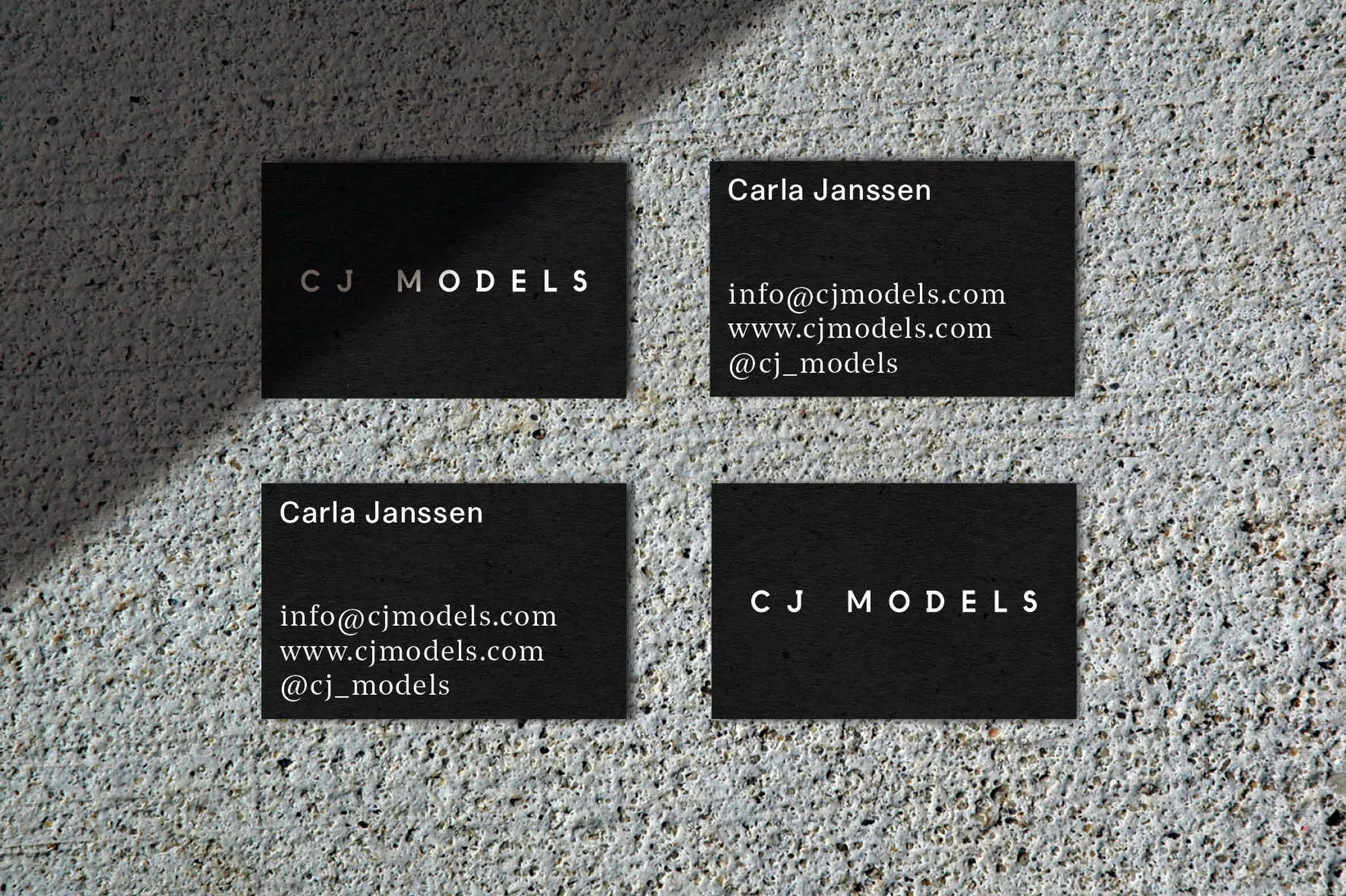 Close-up of four black business cards with the text 'CJ Models' and contact information on a textured grey background with shadow.