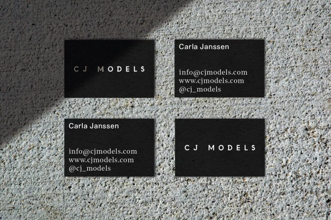 Four black business cards with white text arranged on a textured concrete surface under diagonal sunlight.