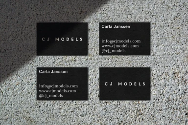 Four black business cards with white text arranged on a textured concrete surface under diagonal sunlight.