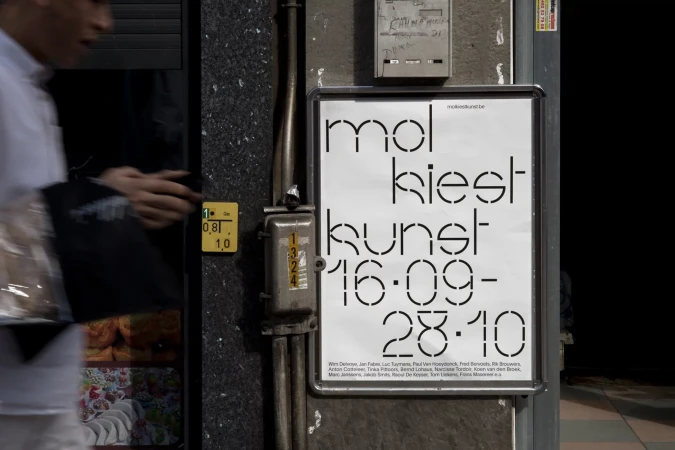 Poster for 'mol kiest kunst 16-09-28-10' affixed to a building's exterior wall, next to electrical boxes and pipes, with pedestrian passing by.