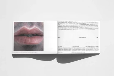 Open art book spread featuring a close-up image of human lips on the left page and descriptive typography on the right.