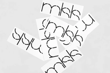Overhead view of overlapping white rectangular labels featuring custom black stencil typography on a light gray textured background.