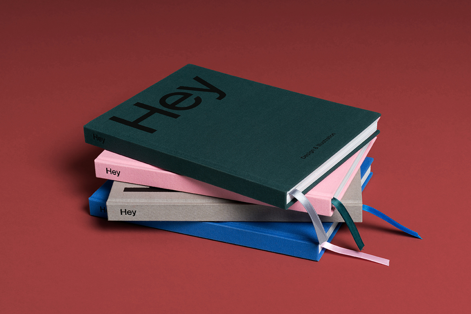 Stack of colorful hardback notebooks with ribbons, each with the word "Hey" on the cover, on a red background.