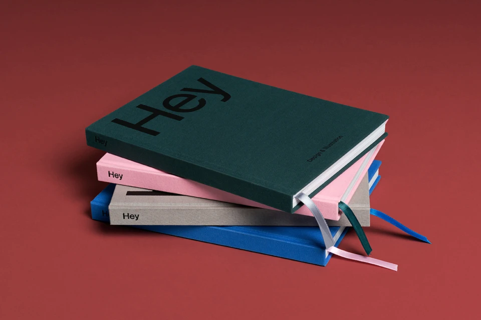 Stack of colorful hardback notebooks with ribbons, each with the word "Hey" on the cover, on a red background.
