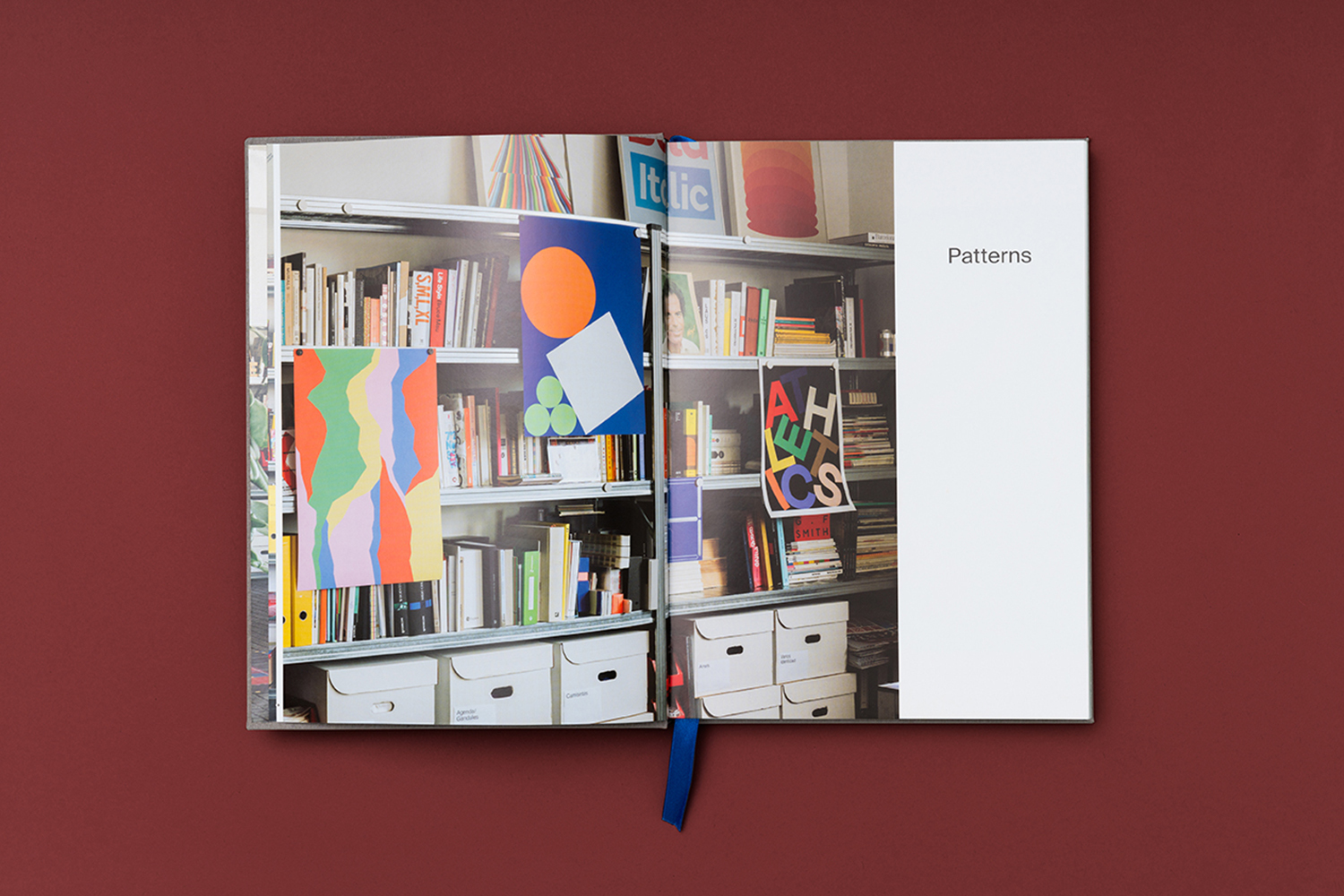 Open book showcasing a photograph of a bookshelf filled with books, paper art, and organizational boxes, viewed on a red surface.