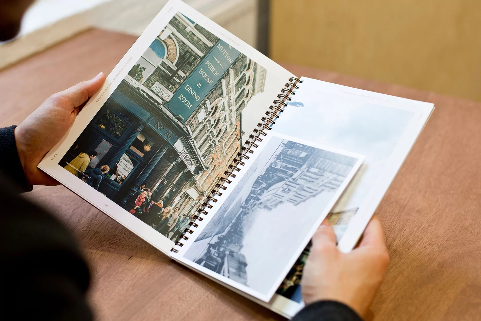 Person holding open a spiral-bound book featuring a color photo of a London pub and a black and white photo of another building.