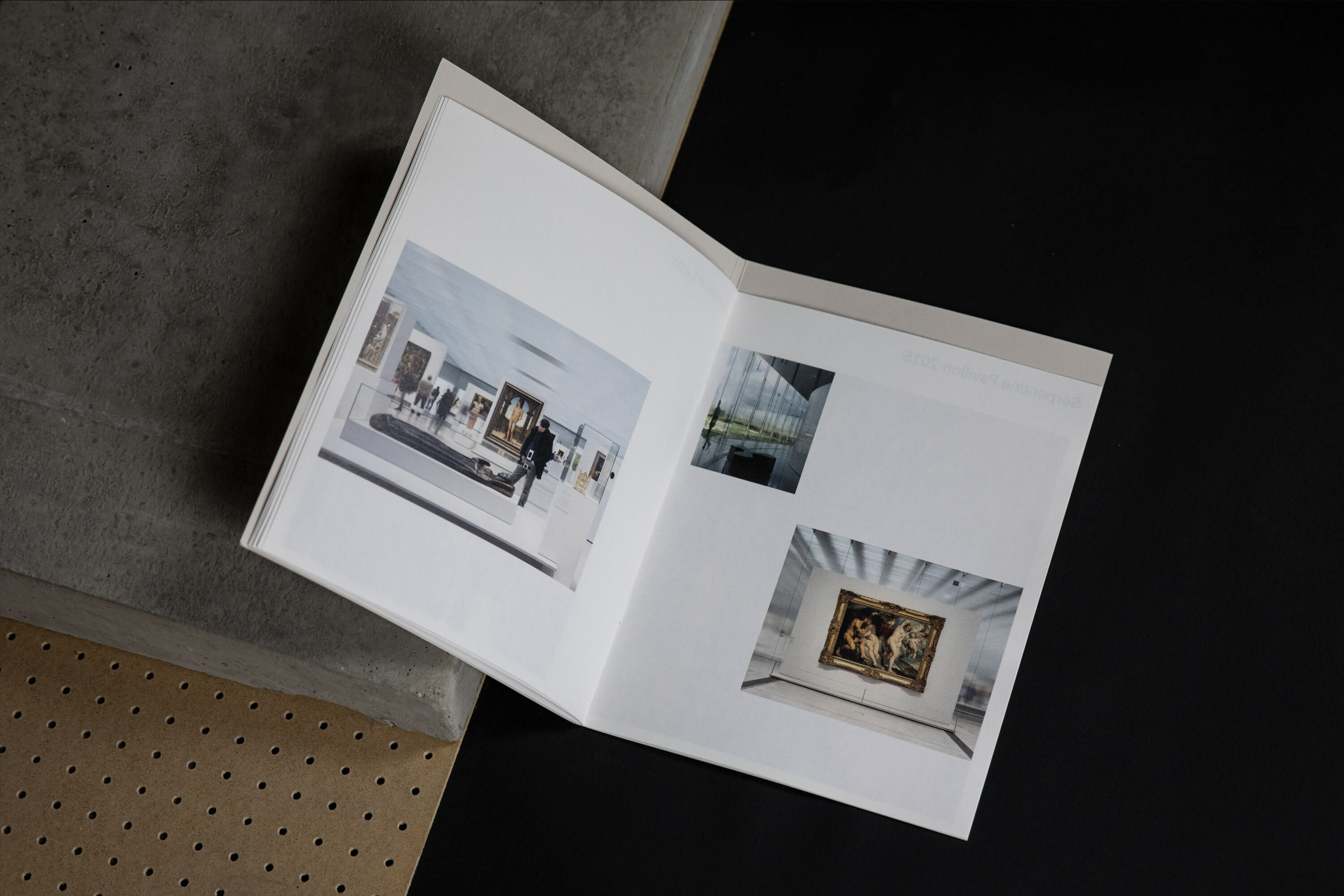 Open book displays photos of museum interiors and modern buildings, resting on grey and black surfaces, showcasing architectural photography.