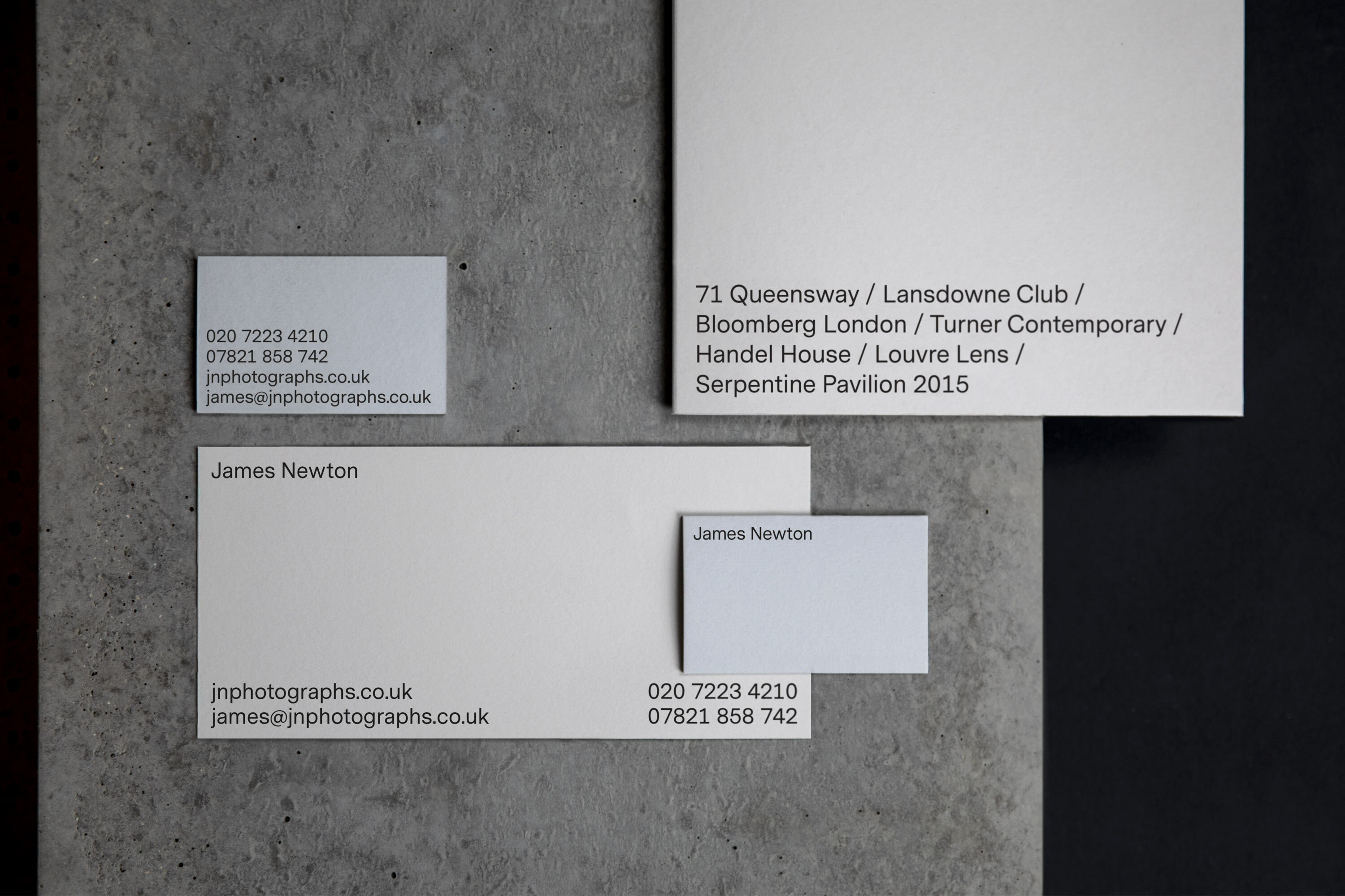 Various business cards with James Newton branding arranged on a textured grey surface with a dark background. Text includes contact info.