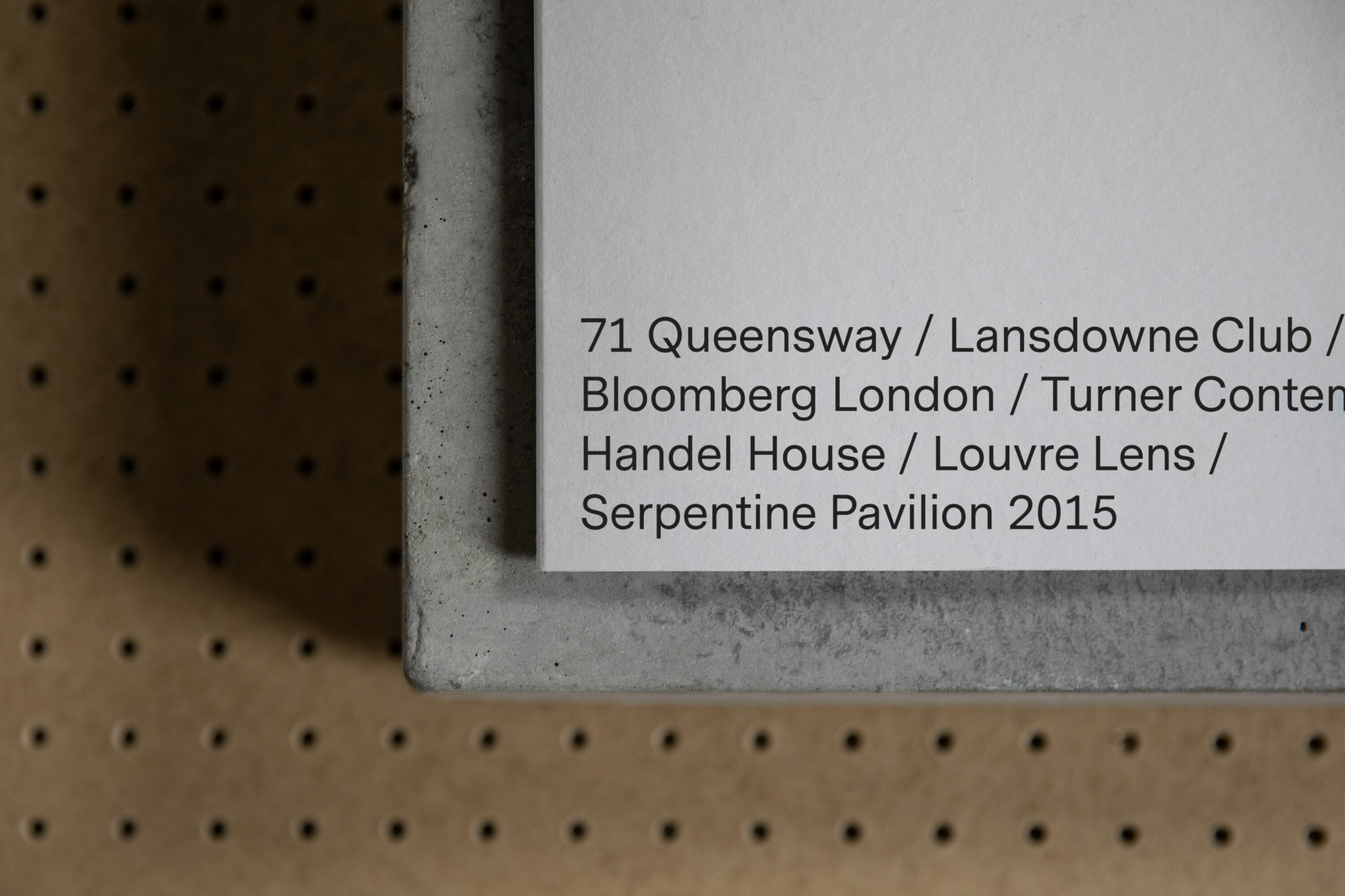 Close-up of a concrete-framed artwork featuring the text: '71 Queensway / Lansdowne Club / Bloomberg London / Turner Contem / Handel House'