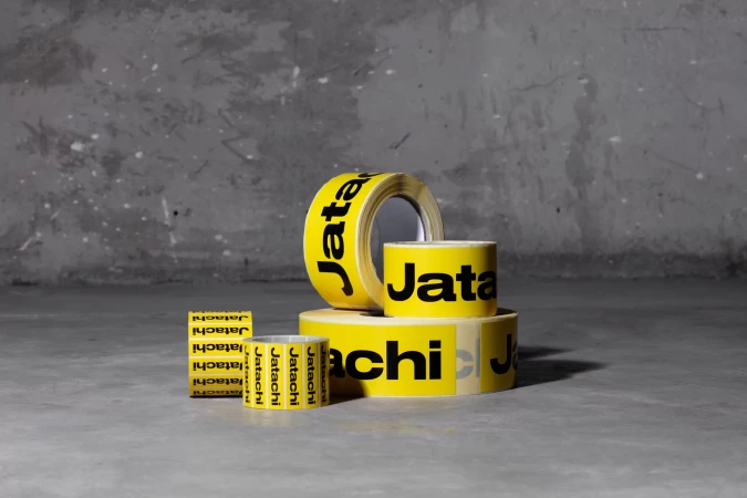 Rolls of yellow packaging tape with black lettering and a neutral grey backdrop create a minimalist product presentation.