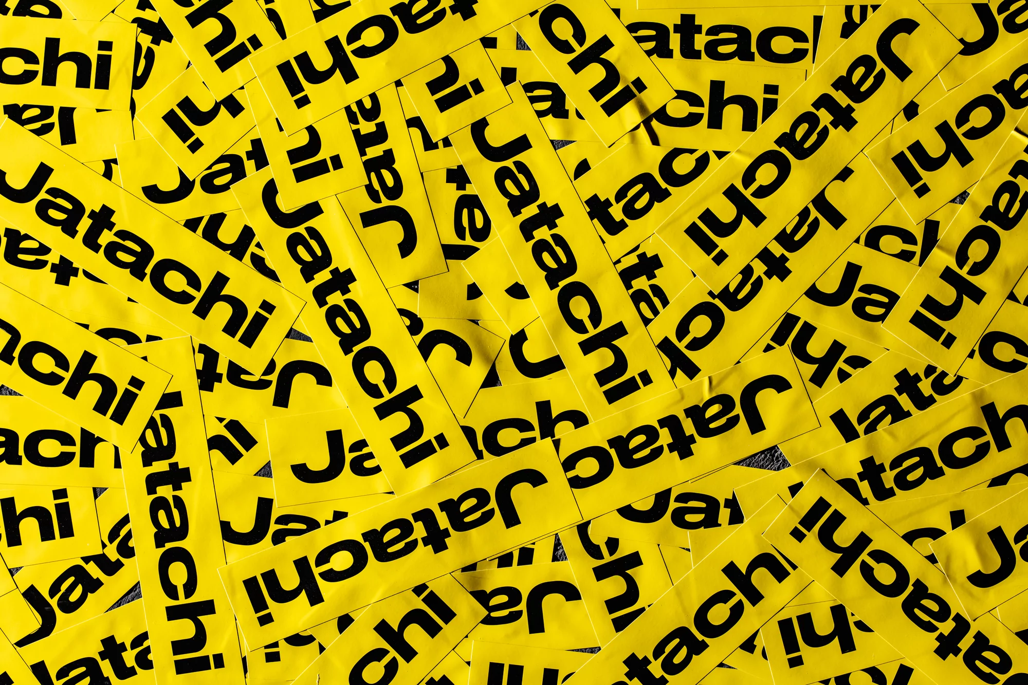 A high-angle, full-frame shot shows numerous yellow rectangular stickers, closely packed together, each displaying the black text 'Jatachi'.