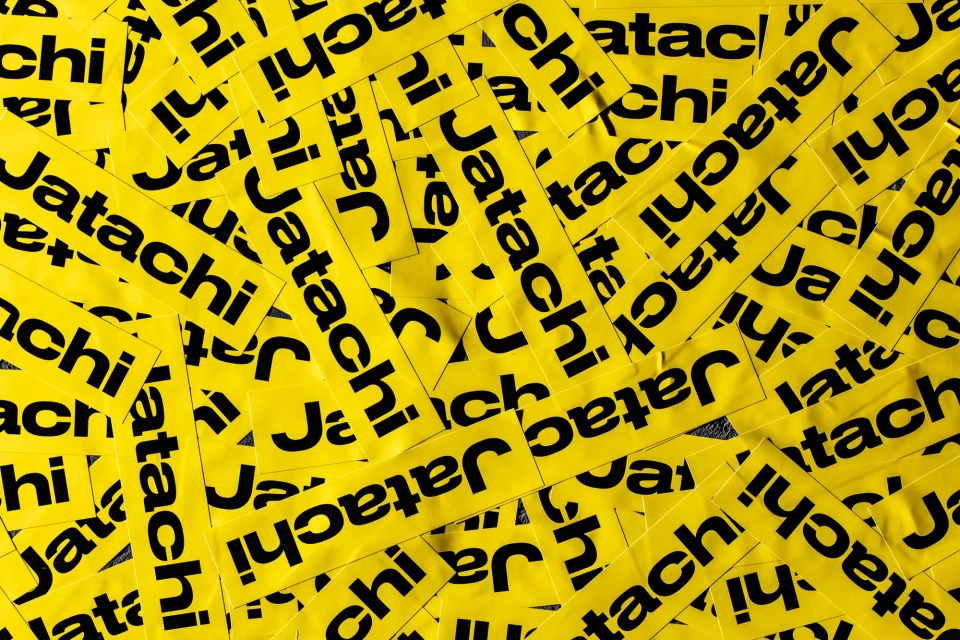 A high-angle, full-frame shot shows numerous yellow rectangular stickers, closely packed together, each displaying the black text 'Jatachi'.