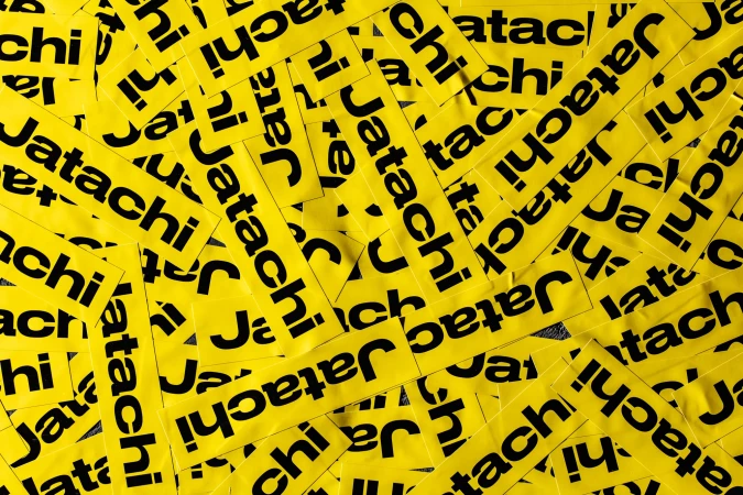 A high-angle, full-frame shot shows numerous yellow rectangular stickers, closely packed together, each displaying the black text 'Jatachi'.