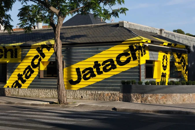 Exterior shot of a commercial building featuring a facade with a gray corrugated metal and stone base, marked with bold yellow and black stripes.