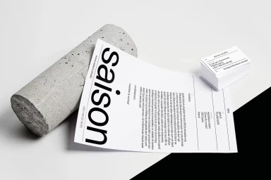 Minimalist brand identity layout featuring printed stationery and a cylindrical concrete prop on white surface