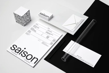 Minimalist brand identity layout featuring Saison stationery, business cards, invoice, envelope, and graphic cube on a monochrome background