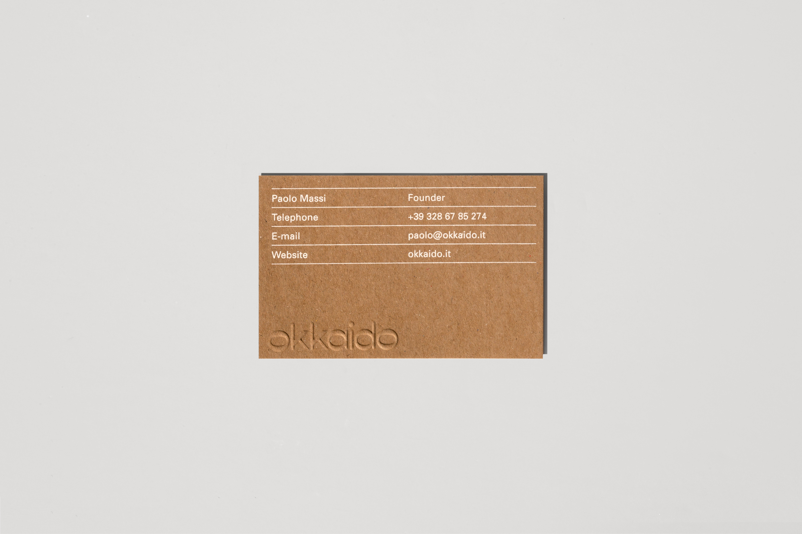 Close-up of a brown business card with white text featuring contact information, including name, title, phone number, email, and website.