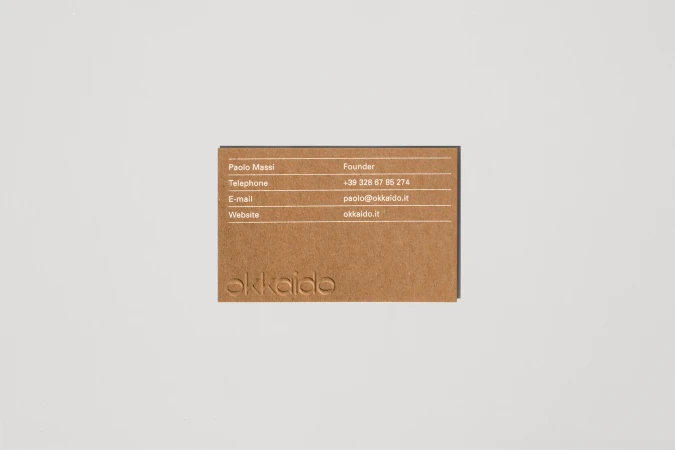Close-up of a brown business card with white text featuring contact information, including name, title, phone number, email, and website.