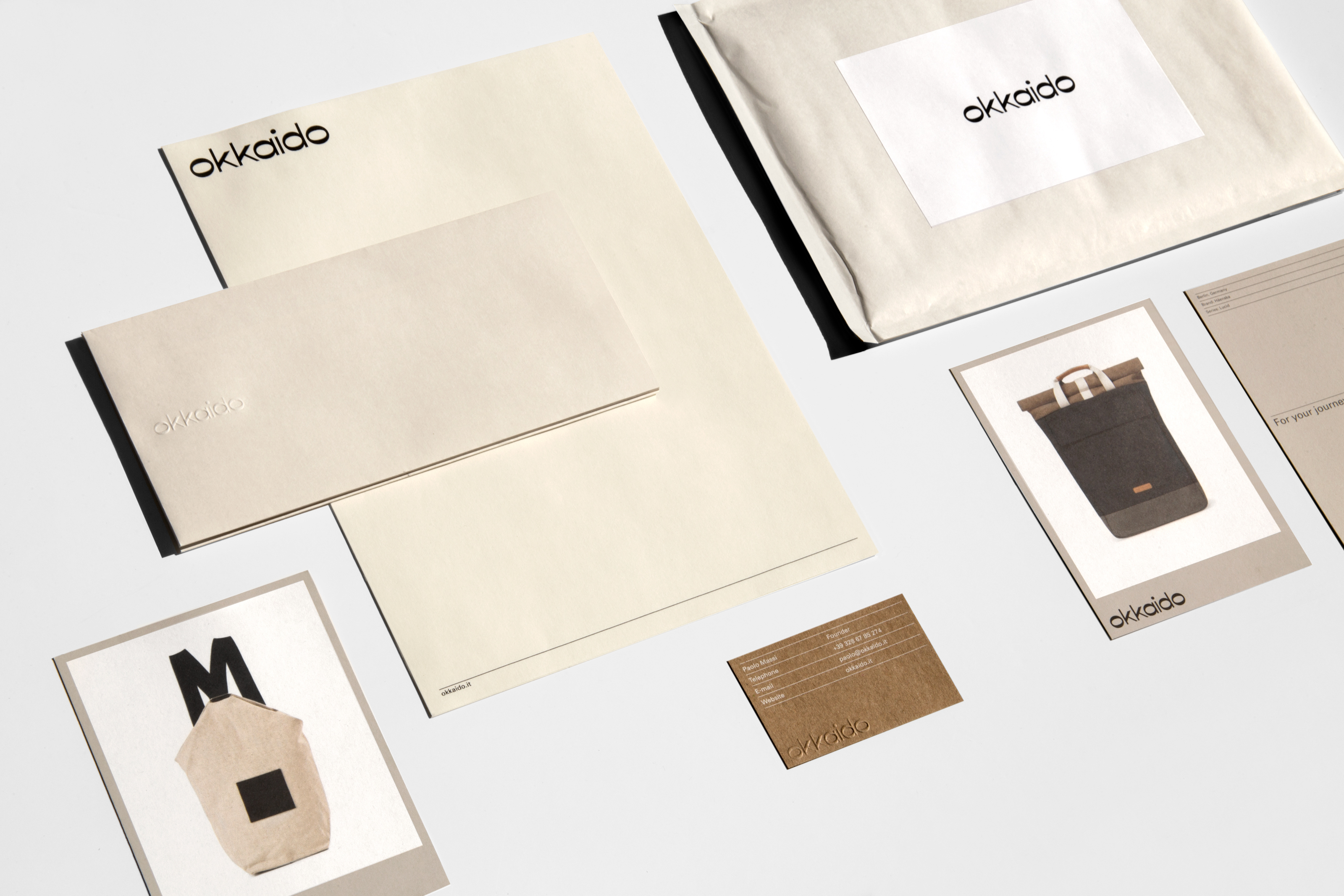 Arrangement of stationery and cards, featuring the 'okkaido' logo, displayed on a clean white surface with minimalist branding elements.