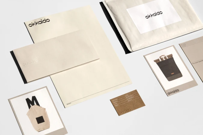 Arrangement of stationery and cards, featuring the 'okkaido' logo, displayed on a clean white surface with minimalist branding elements.