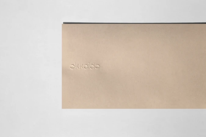 Studio shot of a minimalistic beige book with a dark trim, resting on a white surface, featuring subtle embossing.