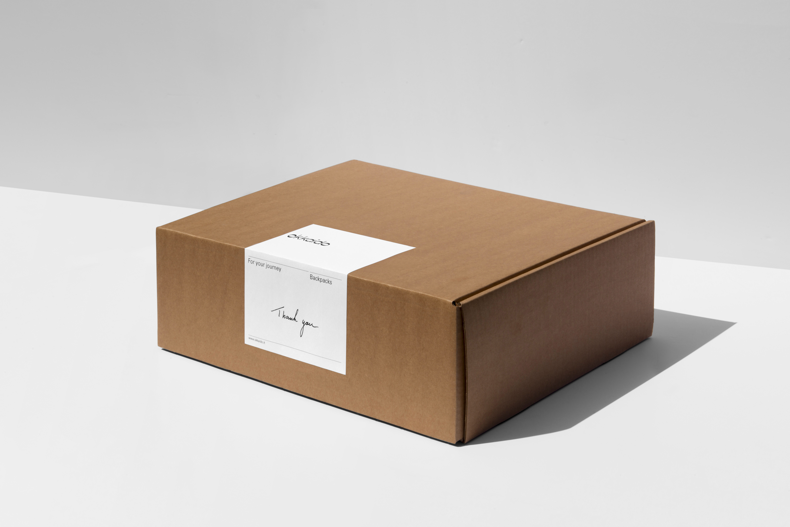 Brown cardboard box with white label displaying product information and a thank you message, set against a neutral backdrop.